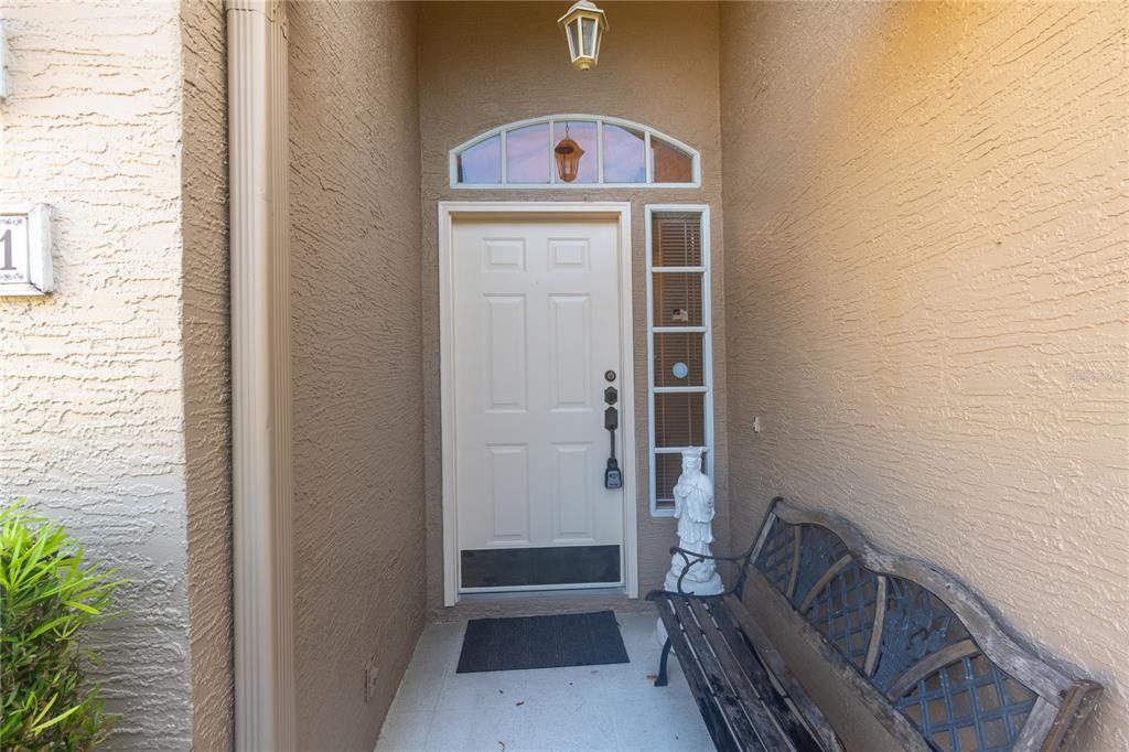 A front entryway features a white door with a sidelight, a bench, and stucco walls — 7541 MOORGATE COURT, NEW PORT RICHEY, FL