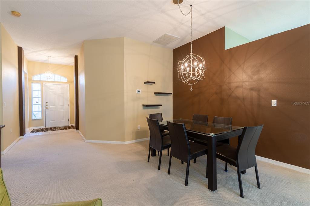 A dining room features a glass-topped table, dark chairs, a modern chandelier, and brown walls — 7541 MOORGATE COURT, NEW PORT RICHEY, FL