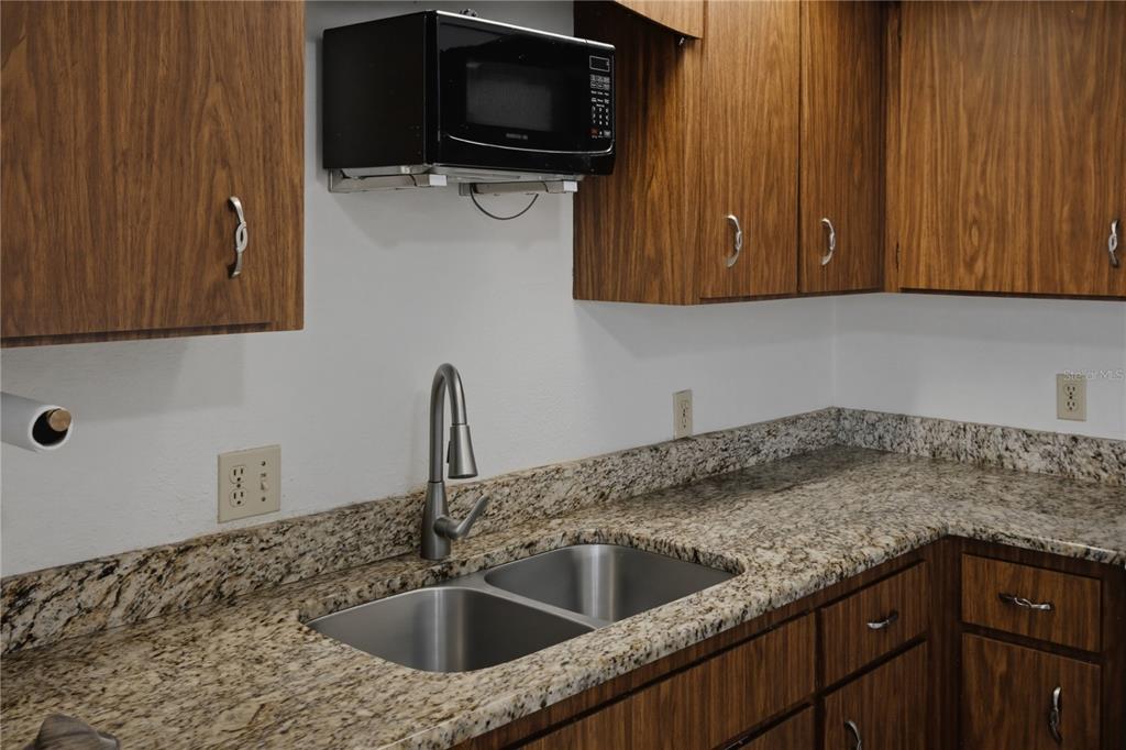 A kitchen features wood cabinets, granite countertops, a double-basin sink, and a mounted microwave — 101 LAKE HUNTER DRIVE UNIT 11, LAKELAND, FL