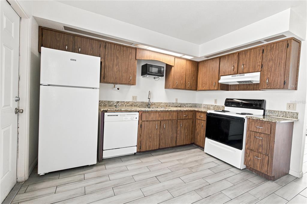 A kitchen features wood cabinets, granite countertops, white appliances, and light-colored wood-look tile flooring — 101 LAKE HUNTER DRIVE UNIT 11, LAKELAND, FL