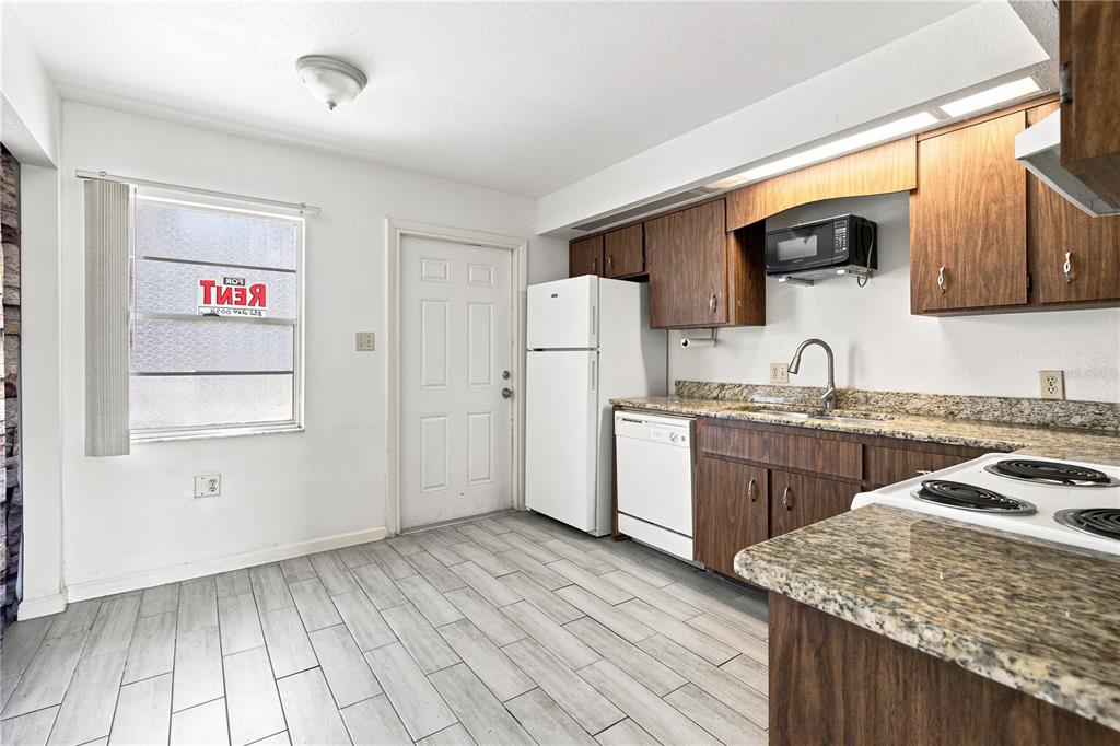 A kitchen features wood cabinets, granite countertops, white appliances, and light-colored tile flooring — 101 LAKE HUNTER DRIVE UNIT 11, LAKELAND, FL