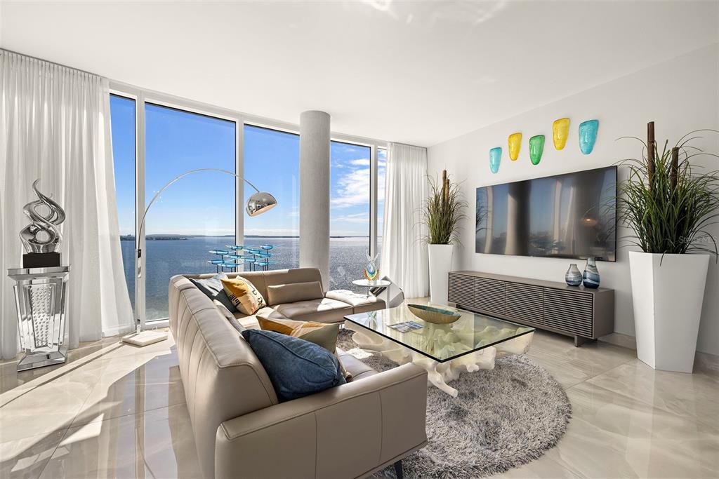 A modern living room features a beige sectional, glass coffee table, and floor-to-ceiling water views — 2900 W BAY TO BAY BOULEVARD UNIT 1403, TAMPA, FL
