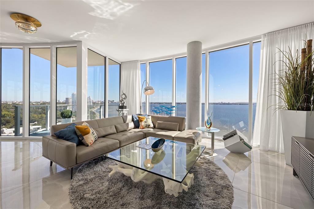 A modern living room features a sectional sofa, glass coffee table, and floor-to-ceiling windows overlooking water — 2900 W BAY TO BAY BOULEVARD UNIT 1403, TAMPA, FL
