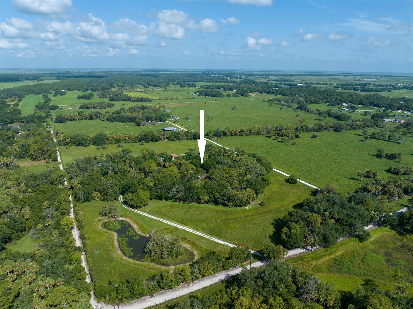 An aerial view shows a wooded property with a pond and dirt roads in Florida — 13500 NW 2nd Avenue, Okeechobee FL 34972, OKEECHOBEE, FL