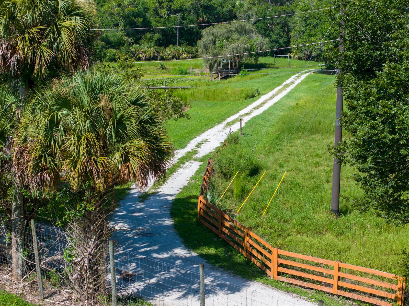 An aerial view shows a gravel driveway winding through a grassy field past a wooden fence — 13500 NW 2nd Avenue, Okeechobee FL 34972, OKEECHOBEE, FL