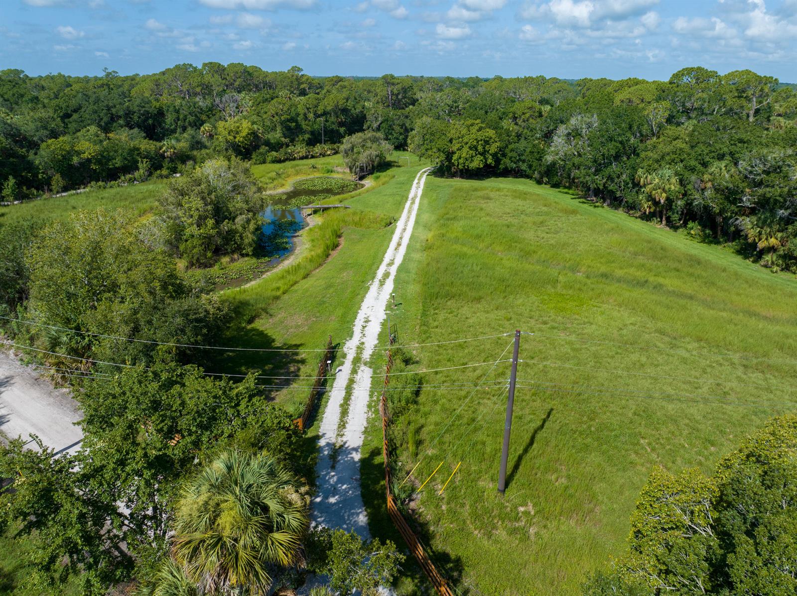 An aerial view shows a gravel driveway leading through a grassy field toward a pond — 13500 NW 2nd Avenue, Okeechobee FL 34972, OKEECHOBEE, FL