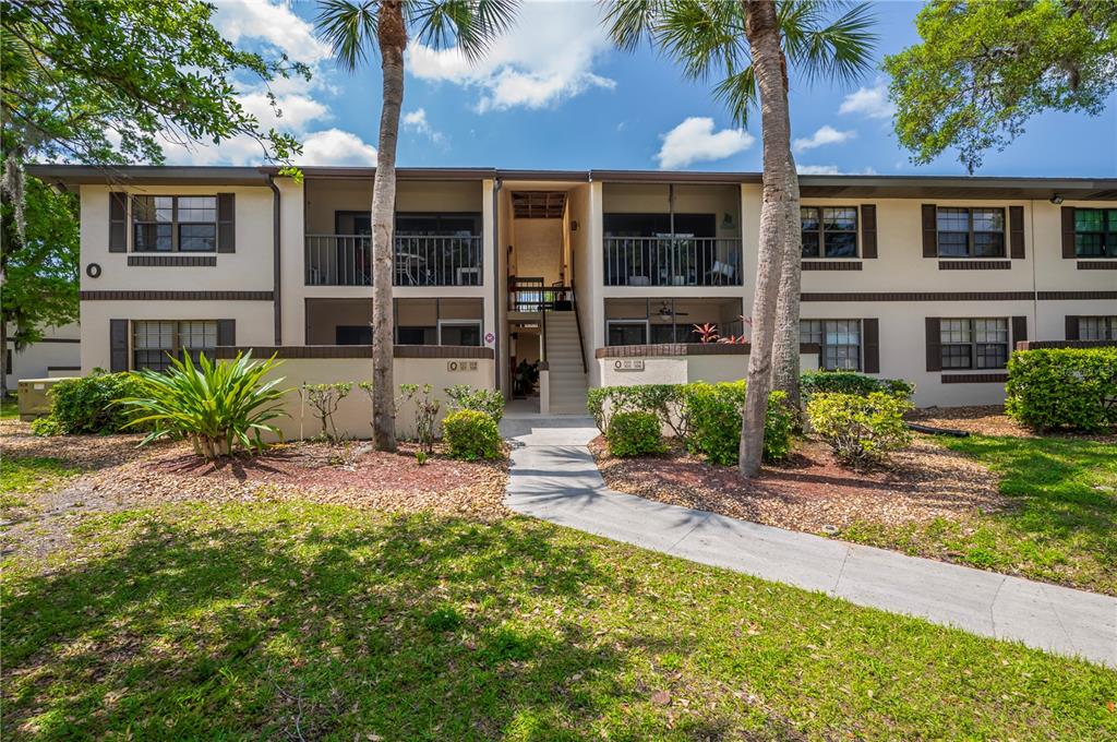 A two-story apartment building features a central staircase, balconies, and palm trees in front — 19505 QUESADA AVENUE UNIT O207, PORT CHARLOTTE, FL