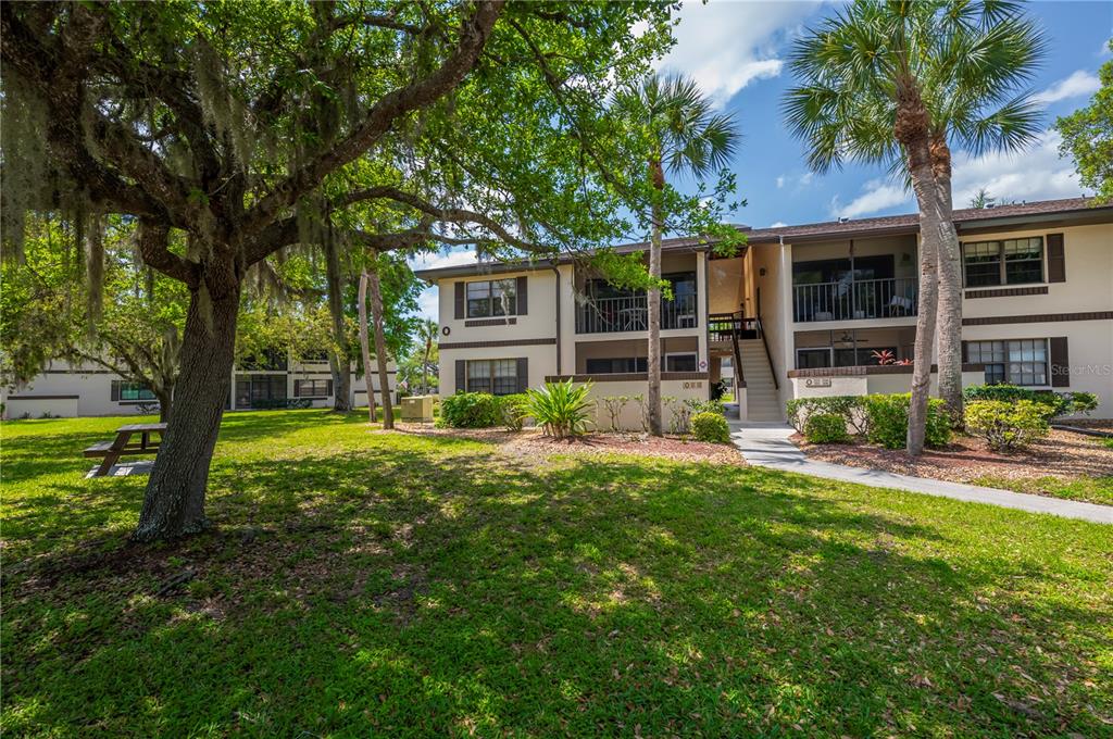 A two-story apartment building with a grassy lawn, large oak trees, and palm trees — 19505 QUESADA AVENUE UNIT O207, PORT CHARLOTTE, FL
