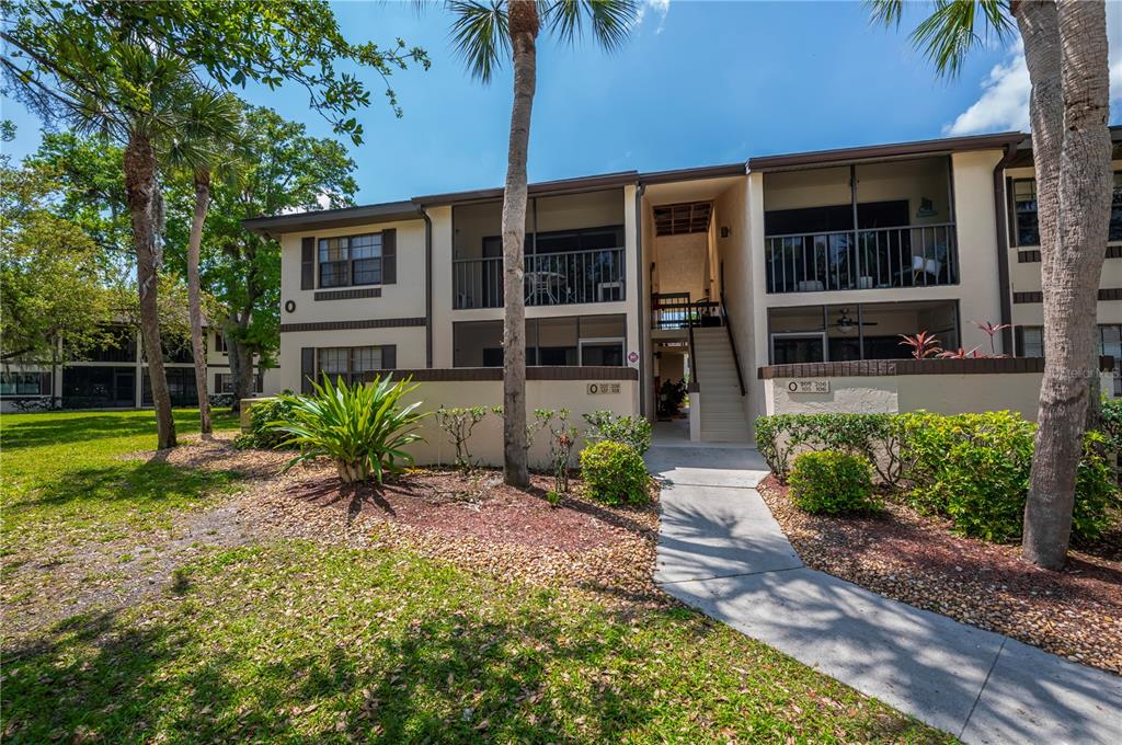 A two-story apartment building features screened balconies, a central staircase, and surrounding landscaping — 19505 QUESADA AVENUE UNIT O207, PORT CHARLOTTE, FL