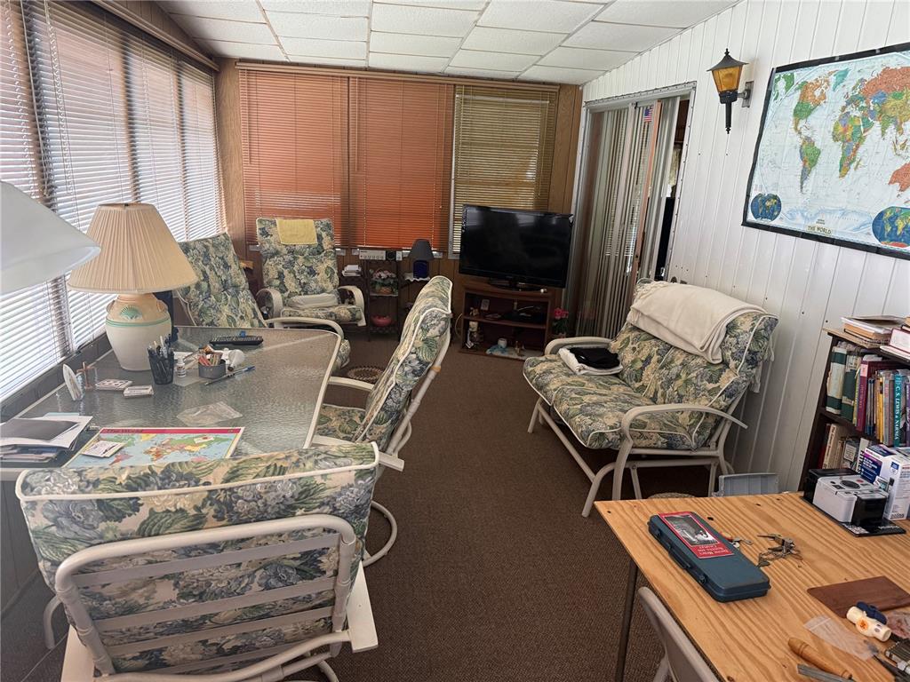 A sunroom features a glass-top dining table, floral-patterned chairs, a television, and a world map — 7256 WINDY WAY, BROOKSVILLE, FL