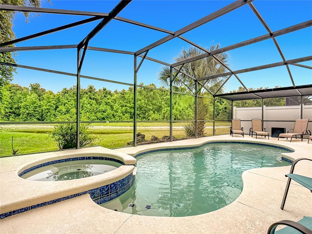 A screened-in pool and spa area overlooks a grassy yard and a line of trees — 522 SANDY RIDGE DRIVE, DAVENPORT, FL