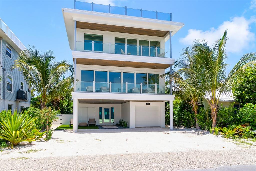 A modern three-story white house with glass balconies and a ground-level garage — 870 N SHORE DRIVE, ANNA MARIA, FL