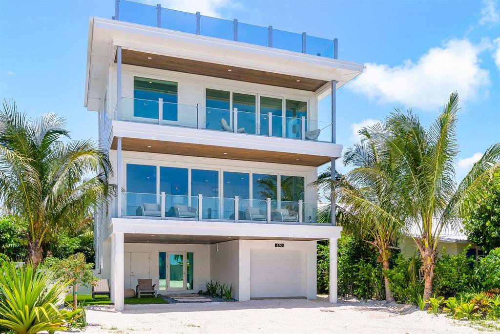 A three-story modern house with glass balconies, a ground-level garage, and surrounding palm trees — 870 N SHORE DRIVE, ANNA MARIA, FL