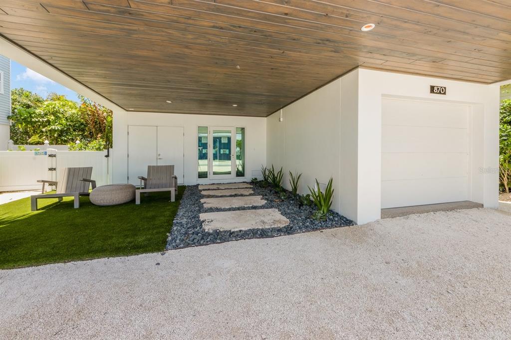 A modern home exterior features a covered entryway, stone pavers, artificial turf, and a garage — 870 N SHORE DRIVE, ANNA MARIA, FL
