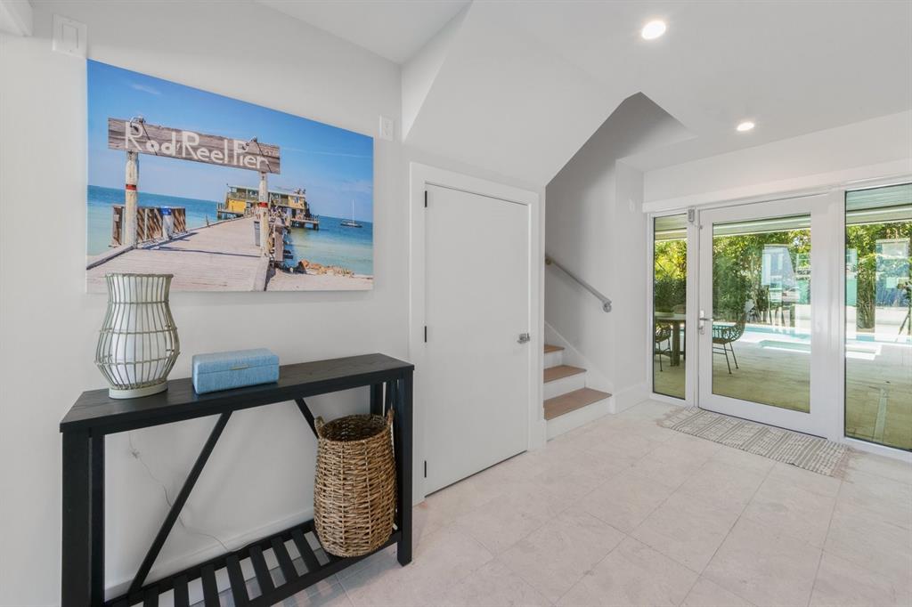 A bright entryway features a black console table, a staircase, and glass doors leading outside — 870 N SHORE DRIVE, ANNA MARIA, FL