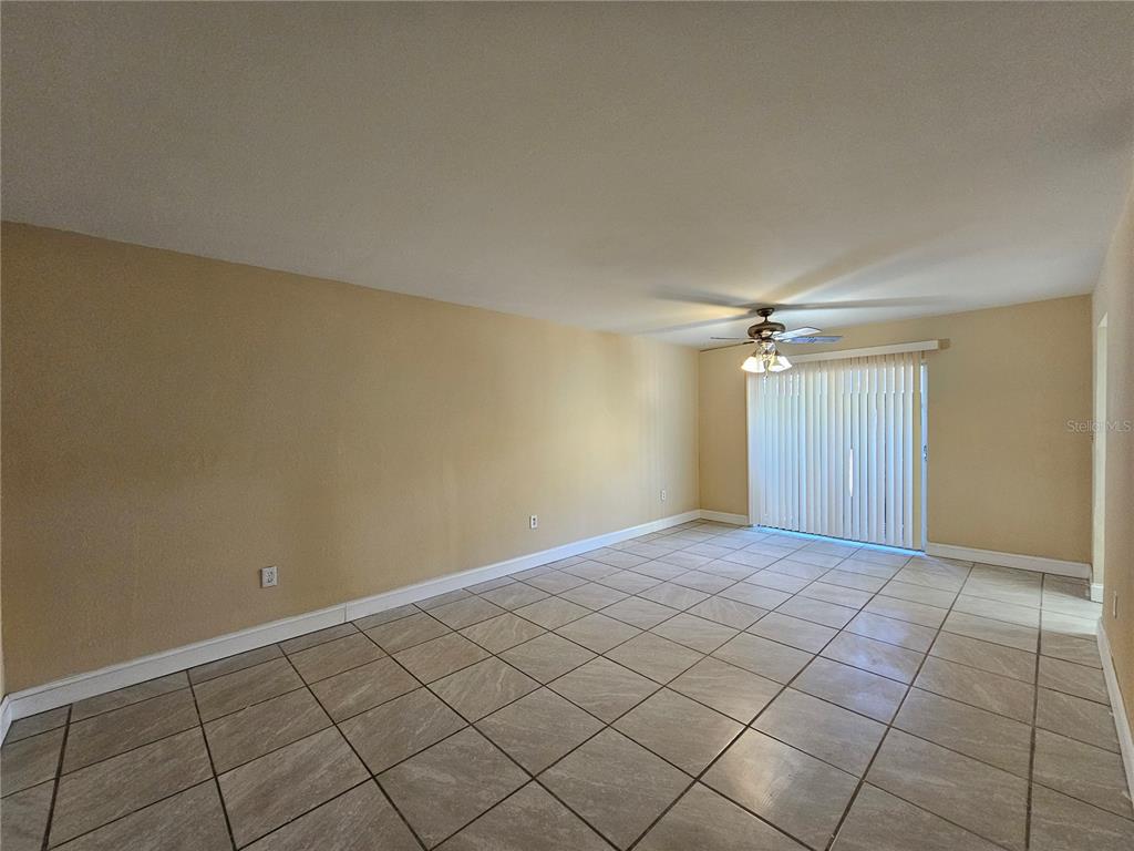 An empty living room features beige walls, large square floor tiles, and a sliding glass door — 7601 PAULA DRIVE UNIT 3, TAMPA, FL