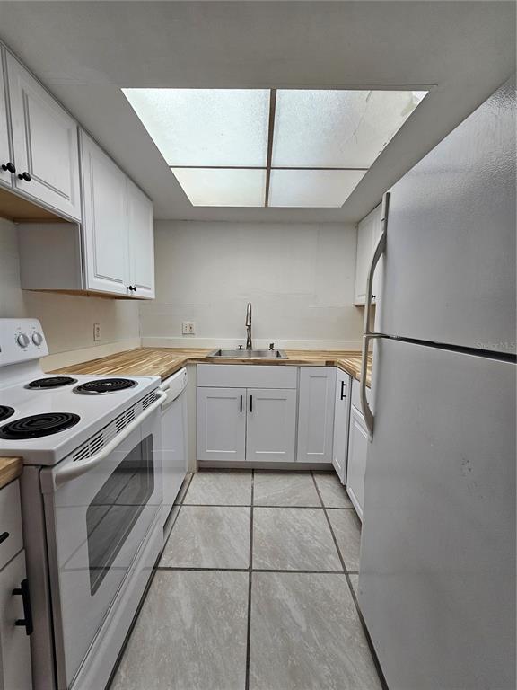A galley kitchen features white cabinets, butcher block countertops, a skylight, and white appliances — 7601 PAULA DRIVE UNIT 3, TAMPA, FL