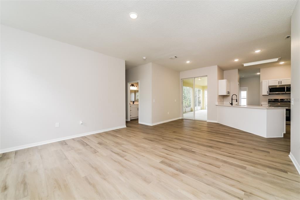 An open-concept living area with light wood-look flooring, white walls, and an adjacent kitchen — 539 BRENTFORD COURT, KISSIMMEE, FL