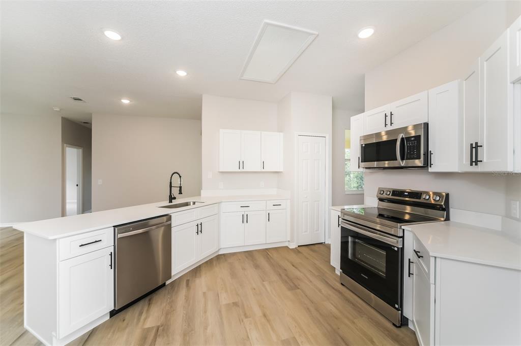 A modern kitchen features white cabinets, stainless steel appliances, and light wood-look flooring — 539 BRENTFORD COURT, KISSIMMEE, FL