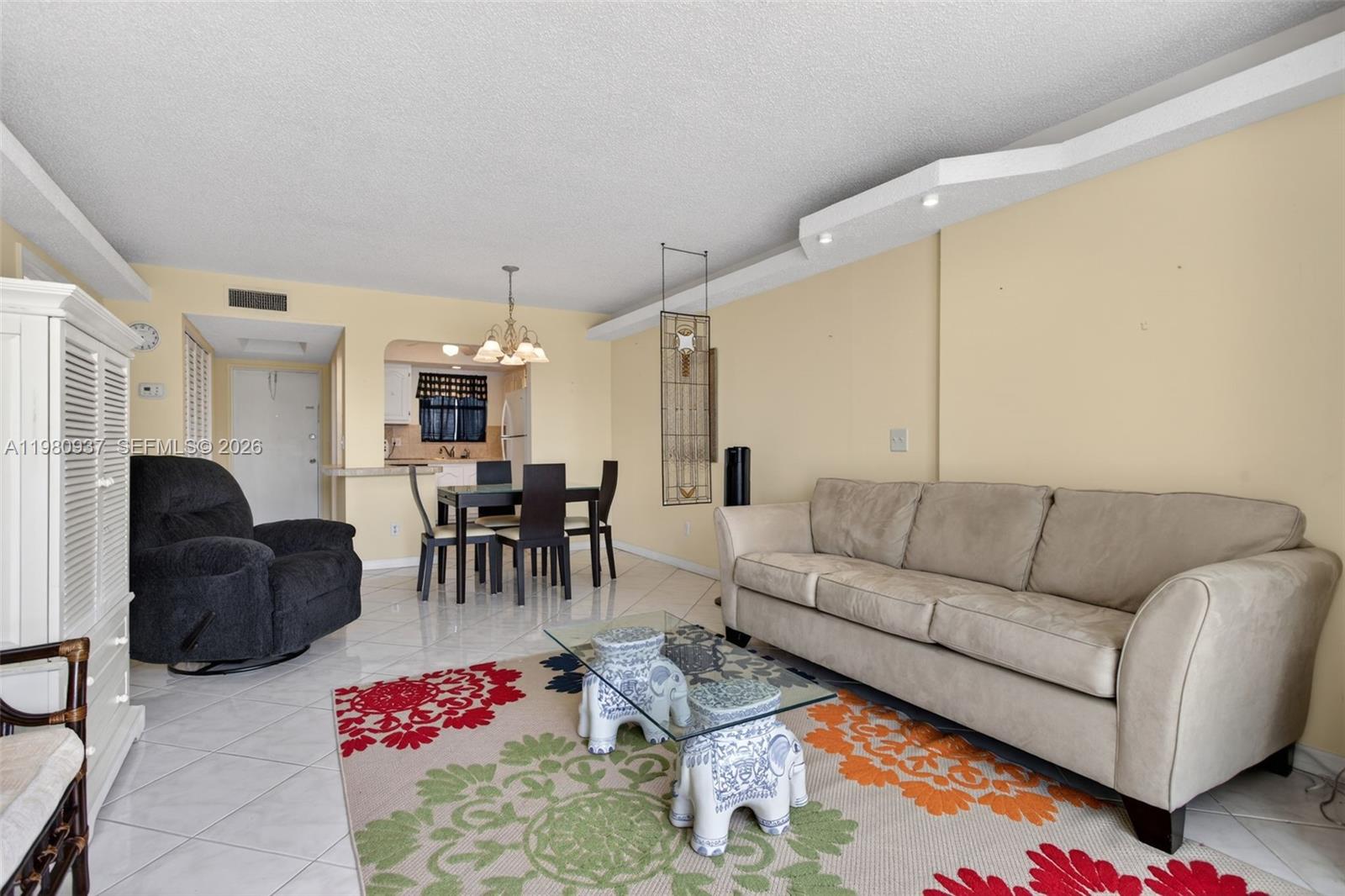 A living room features a beige sofa, a patterned rug, and a dining area nearby — 6600 Royal Palm Blvd # 207B, Margate FL 33063, MARGATE, FL