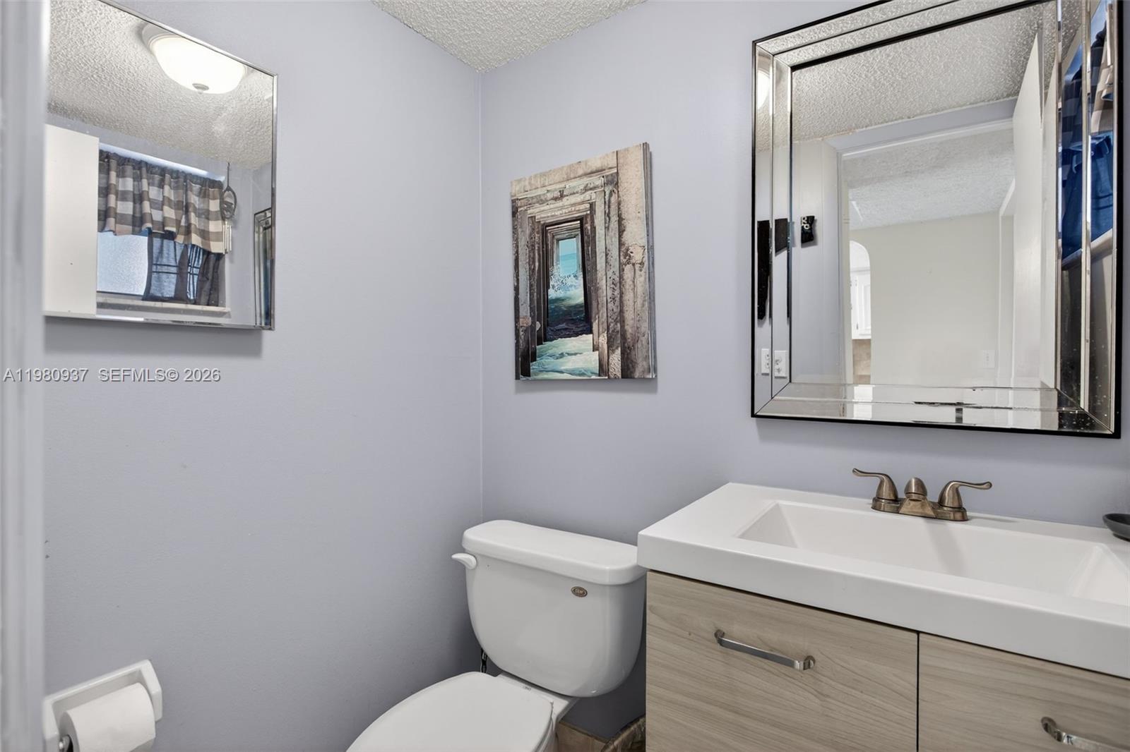 A small bathroom features a vanity with a white sink, a toilet, and two mirrors — 6600 Royal Palm Blvd # 207B, Margate FL 33063, MARGATE, FL