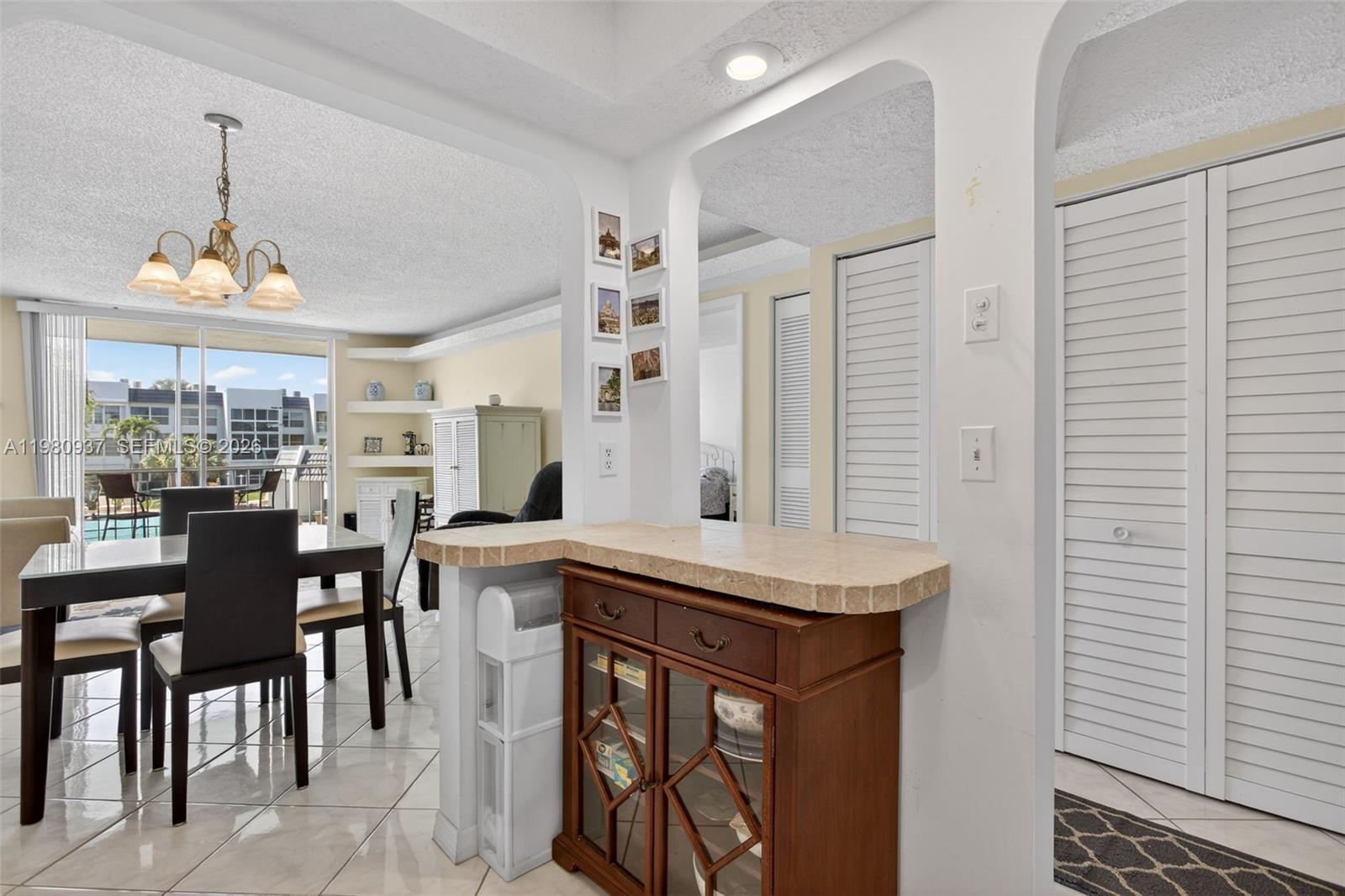 A dining area with a tile floor, chandelier, and a built-in wooden bar counter — 6600 Royal Palm Blvd # 207B, Margate FL 33063, MARGATE, FL