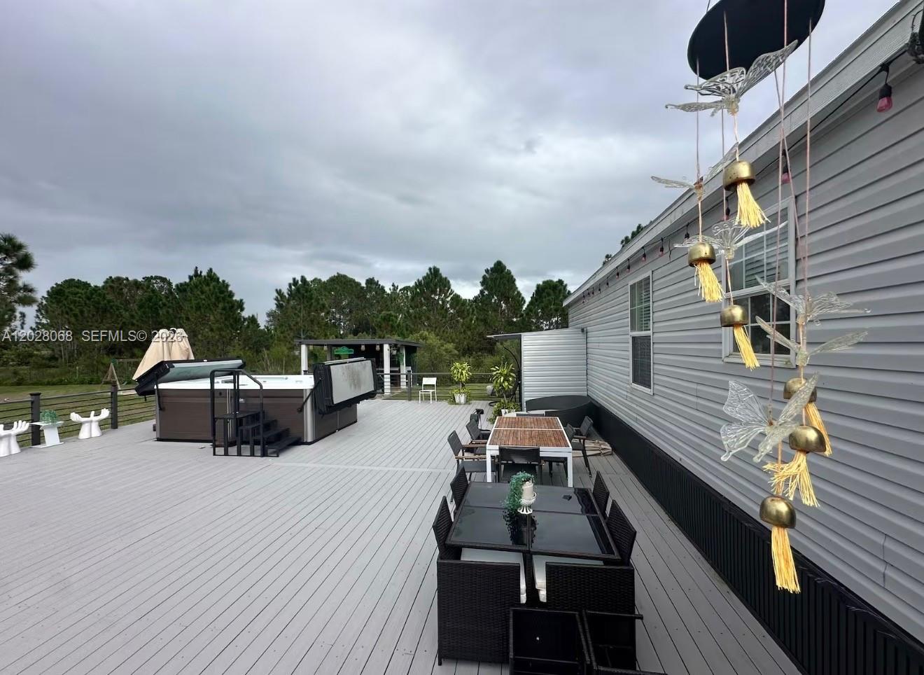 A large outdoor deck features a hot tub, two dining sets, and hanging wind chimes — 17663 NW 266TH ST, Okeechobee FL 34972, OKEECHOBEE, FL
