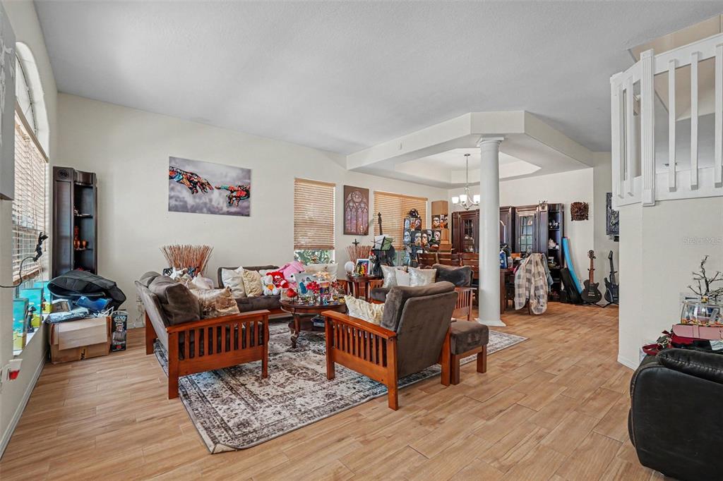 A living room with wood-look tile flooring, a central column, and a dining area beyond — 7212 HAMMET ROAD, TAMPA, FL