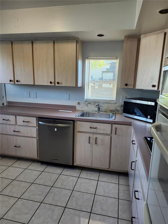A kitchen features light wood cabinets, a stainless steel dishwasher, and white tiled flooring — 2220 BIRCHCREST BOULEVARD, PORT CHARLOTTE, FL