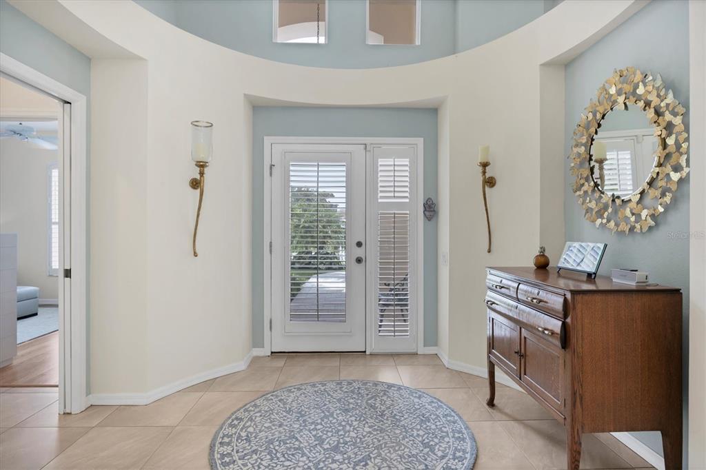 A foyer features a circular rug, a wooden cabinet, a decorative mirror, and arched windows — 7916 HAMPTON COURT, UNIVERSITY PARK, FL