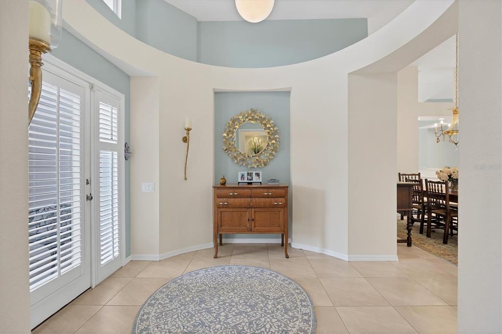 A foyer features a circular rug, a wooden chest, and a decorative mirror on blue walls — 7916 HAMPTON COURT, UNIVERSITY PARK, FL