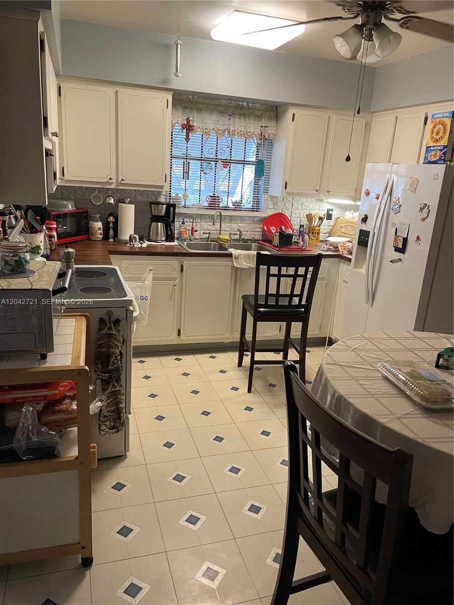 A kitchen features white cabinets, a wood-look countertop, a tiled floor, and a dining table — 1797 NW 113th Ter, Miami FL 33167, MIAMI, FL