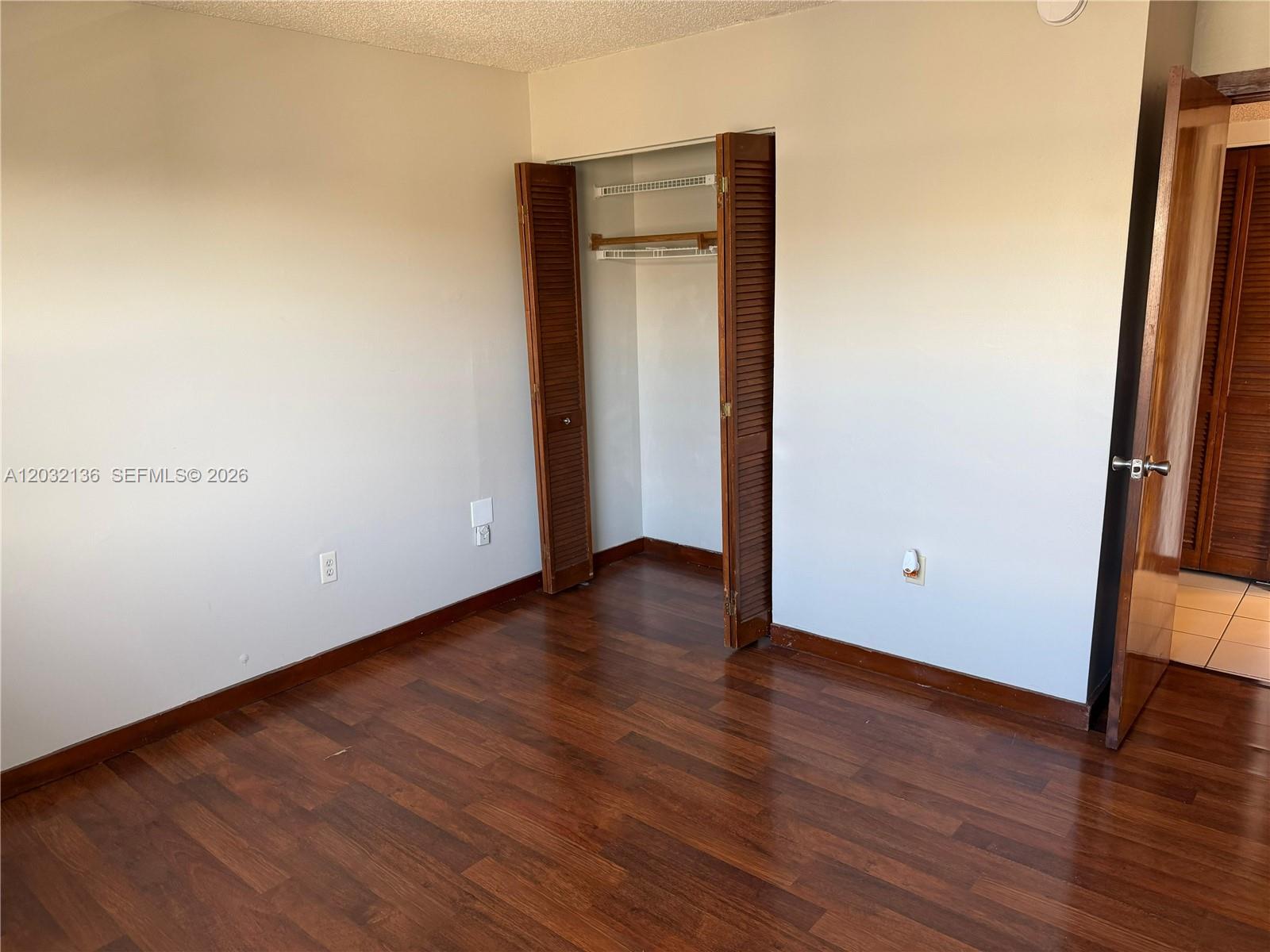 An empty bedroom features dark wood flooring, white walls, and a closet with louvered doors — 605 NW 72nd Ave # 509, Miami FL 33126, MIAMI, FL
