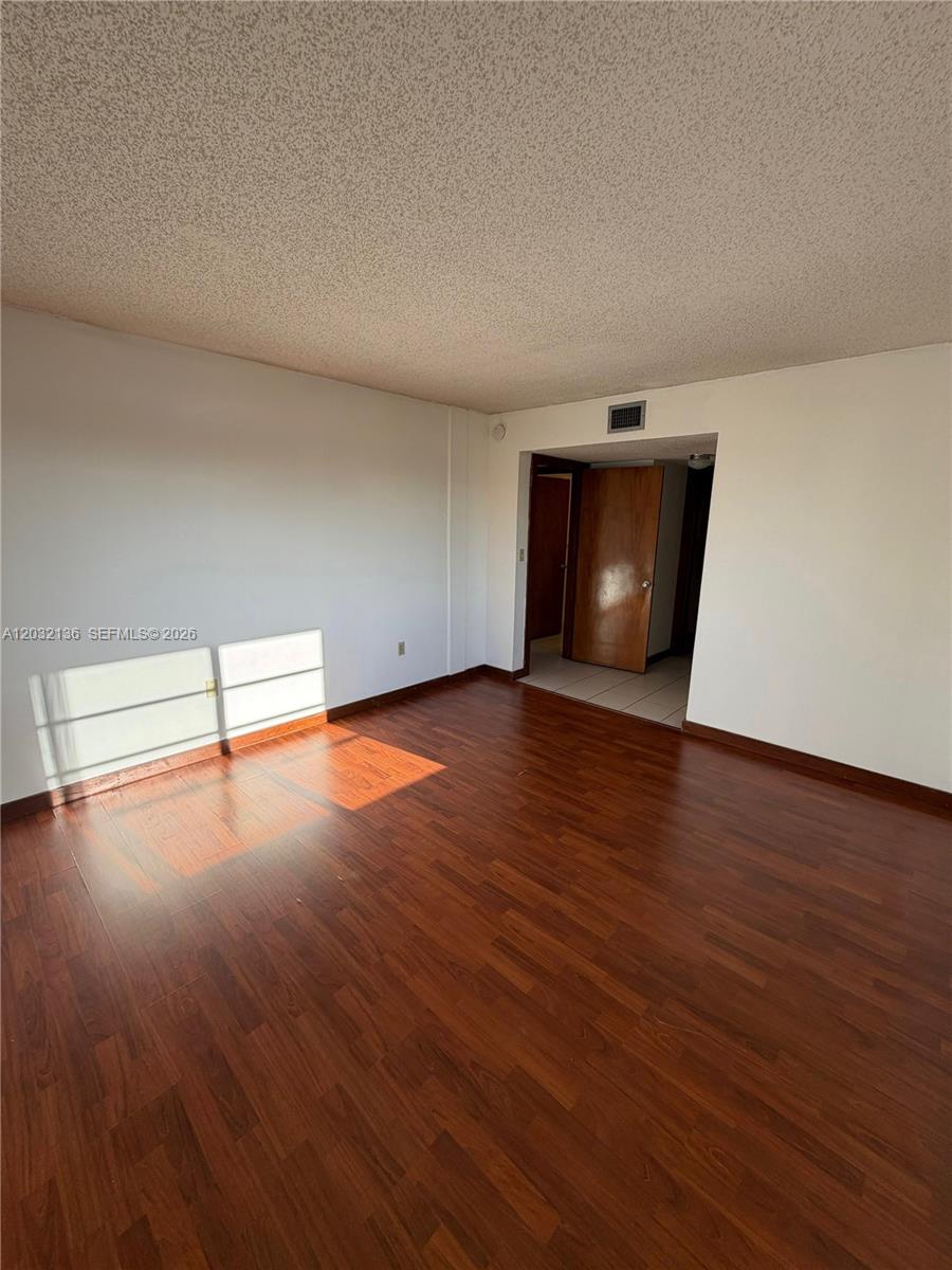 An empty room features dark wood-look flooring, white walls, and a doorway leading elsewhere — 605 NW 72nd Ave # 509, Miami FL 33126, MIAMI, FL