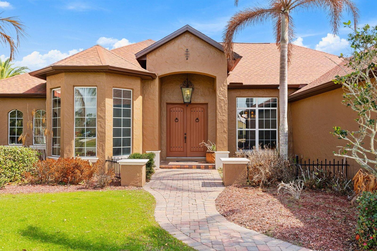 A tan stucco house with a brown shingled roof and a paved walkway to the entrance — MERRITT ISLAND, FL