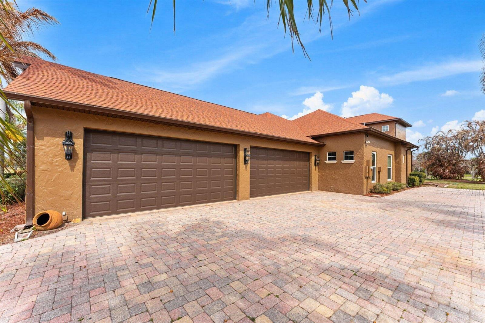 A tan stucco house with a three-car garage and a brick paver driveway — MERRITT ISLAND, FL
