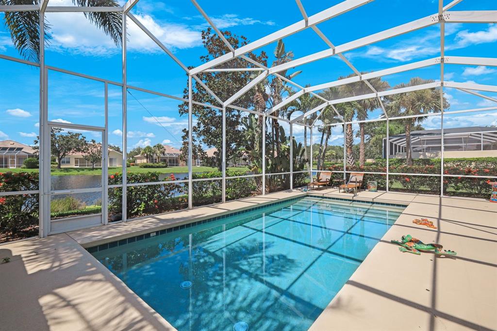 A screened-in swimming pool patio overlooks a lake with palm trees and neighboring houses — 5848 FERRARA DRIVE, SARASOTA, FL