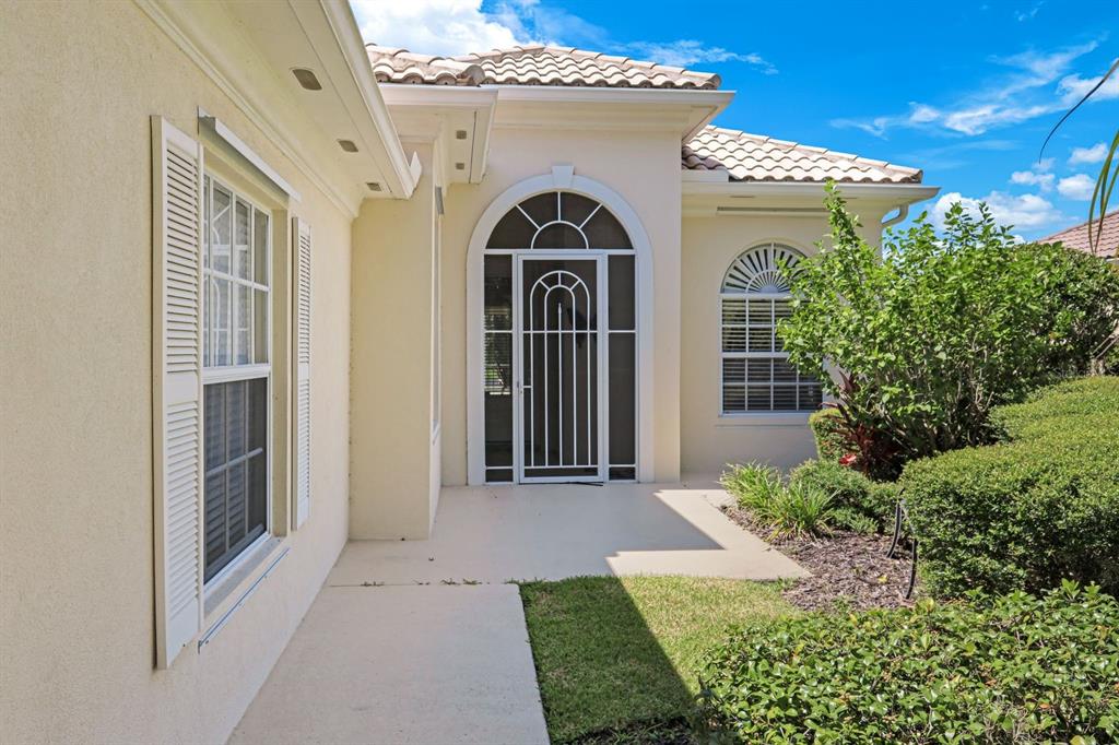 A beige stucco house exterior features a white arched screen door and a tiled roof — 5848 FERRARA DRIVE, SARASOTA, FL