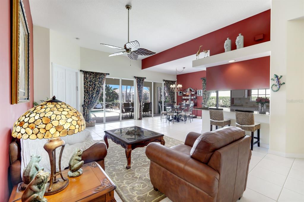 A living room with a leather sofa, armchair, ceiling fan, and views of a pool — 5848 FERRARA DRIVE, SARASOTA, FL