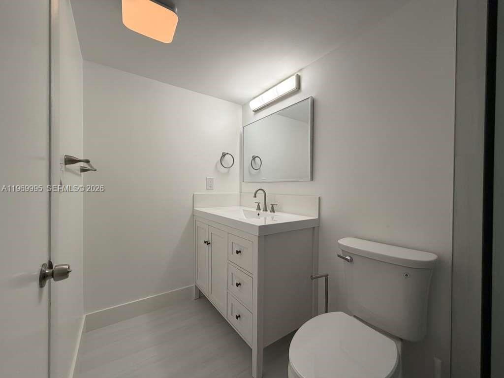 A modern bathroom features a white vanity, a rectangular mirror, and a toilet — 301 SE 3rd St # 109, Dania Beach FL 33004, DANIA BEACH, FL