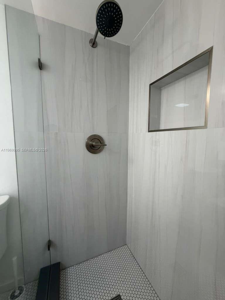 A walk-in shower features light-colored marble-look tile, a black rainfall showerhead, and a recessed niche — 301 SE 3rd St # 109, Dania Beach FL 33004, DANIA BEACH, FL