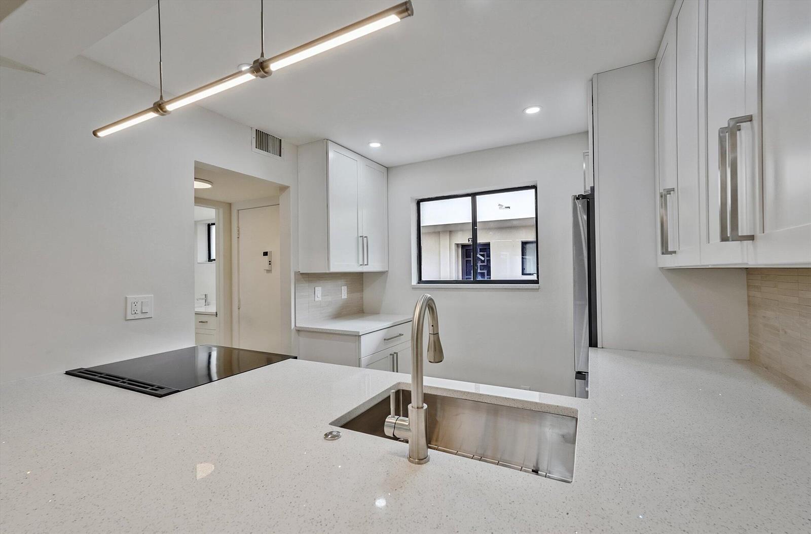 A modern kitchen features white cabinets, quartz countertops, a stainless steel sink, and pendant lighting — 5220 Las Verdes Circle # 321, Delray Beach FL 33484, DELRAY BEACH, FL