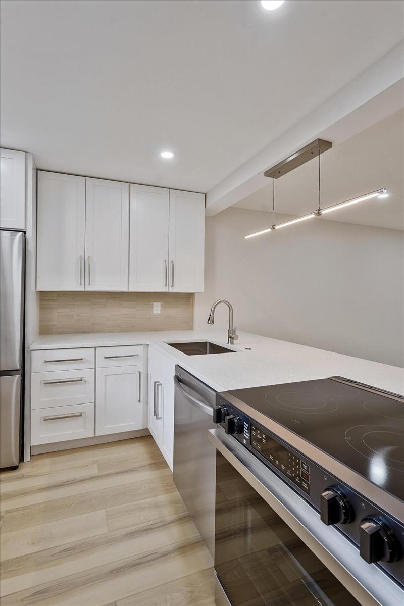 A modern kitchen features white cabinets, stainless steel appliances, and light wood-look flooring — 5220 Las Verdes Circle # 321, Delray Beach FL 33484, DELRAY BEACH, FL