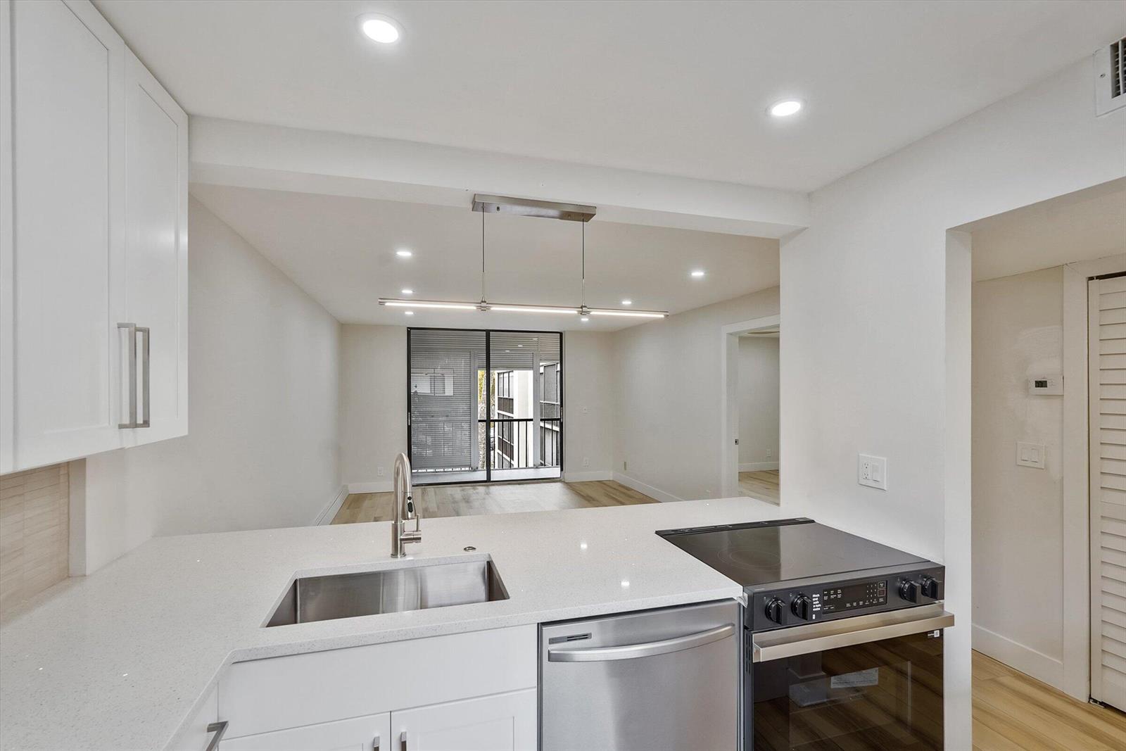 A modern kitchen with white cabinets and stainless steel appliances overlooks an open living area — 5220 Las Verdes Circle # 321, Delray Beach FL 33484, DELRAY BEACH, FL