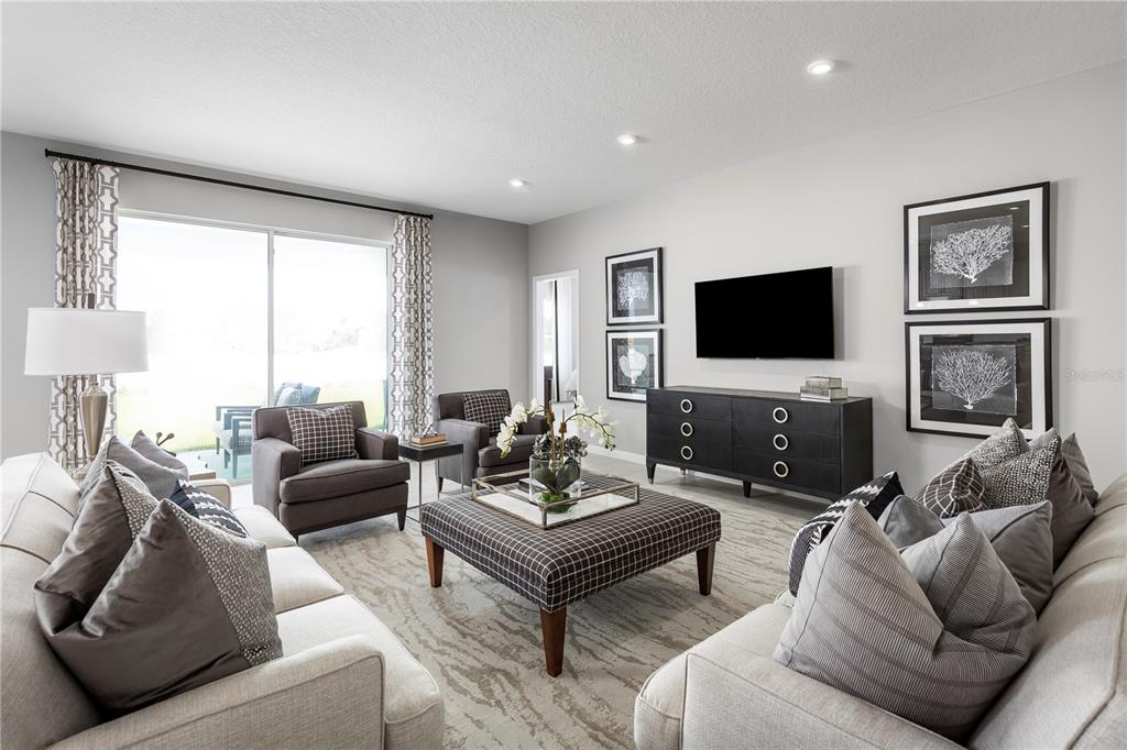 A living room features light-colored sofas, a plaid ottoman, two armchairs, and a wall-mounted television — 9816 PINE MILL COURT, CLERMONT, FL