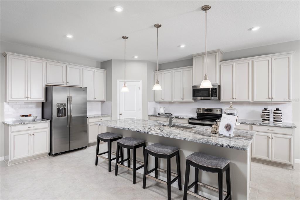 A kitchen with white cabinets, granite countertops, a center island with bar stools, and appliances — 9816 PINE MILL COURT, CLERMONT, FL