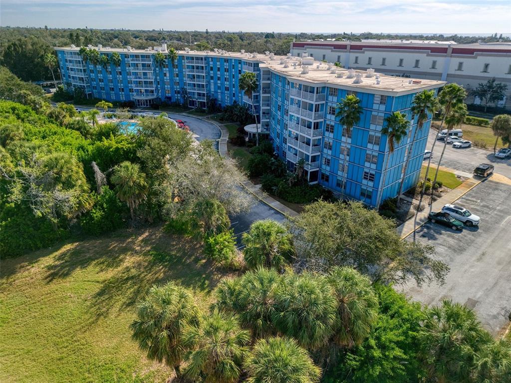 An aerial view shows a multi-story blue apartment building with a pool and parking lot — 3315 58TH AVENUE S UNIT 112, ST PETERSBURG, FL