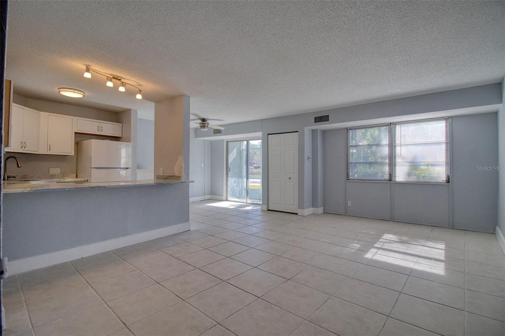 An open-concept living and dining area features light-colored tile floors, white cabinets, and sliding doors — 3315 58TH AVENUE S UNIT 112, ST PETERSBURG, FL