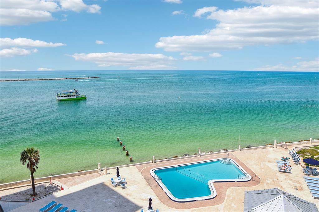 An elevated view of a swimming pool overlooking the ocean with a boat nearby — 450 S GULFVIEW BOULEVARD UNIT 703, CLEARWATER, FL