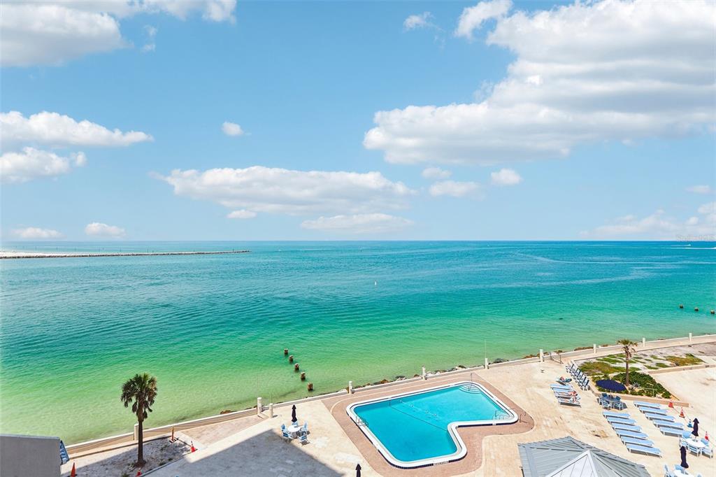 An elevated view of a swimming pool overlooking the ocean and a sandy beach — 450 S GULFVIEW BOULEVARD UNIT 703, CLEARWATER, FL